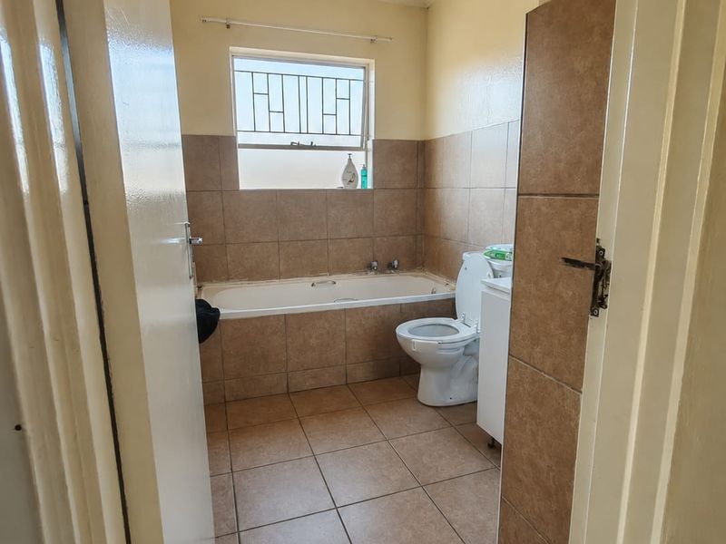 A functional bathroom featuring a bathtub, toilet, and pedestal basin with neutral tiled walls and flooring, offering a clean and practical layout.