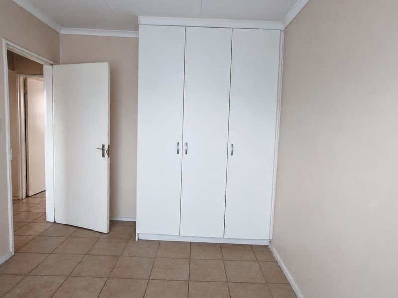 A clean, empty bedroom featuring neutral wall paint, tiled flooring, and a white built-in wardrobe with ample storage space.