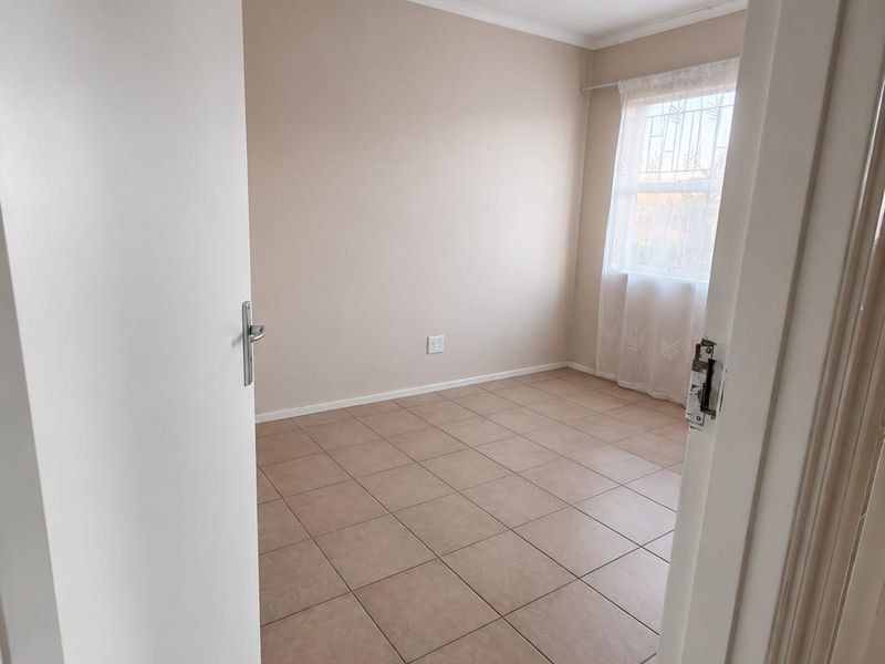 A clean, empty bedroom featuring neutral wall paint, ceramic floor tiles, and a window fitted with security bars.