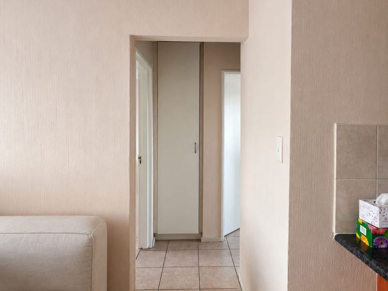 A functional hallway featuring neutral wall finishes, tiled flooring, and a built-in storage cupboard, providing access to adjacent rooms.