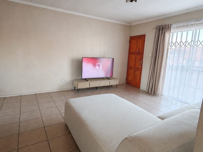 A living room featuring tiled flooring, a ceiling light fixture, and a sliding door with a security gate leading to the exterior.