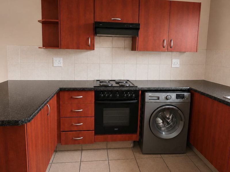 A functional kitchen featuring wood-finish cabinetry, dark laminate countertops, tiled backsplash, and built-in oven with extractor fan.