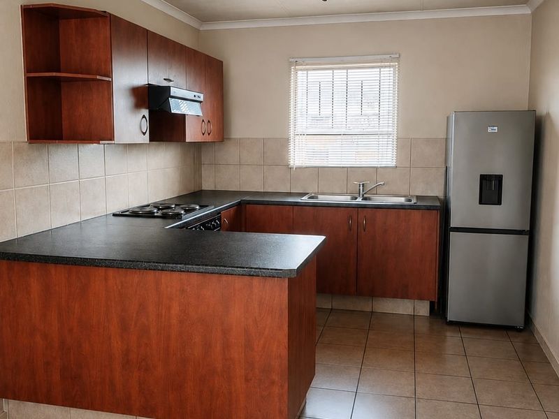 A functional kitchen featuring wood-finish cabinetry, dark laminate countertops, ceramic tile flooring, and a built-in hob with an extractor fan.