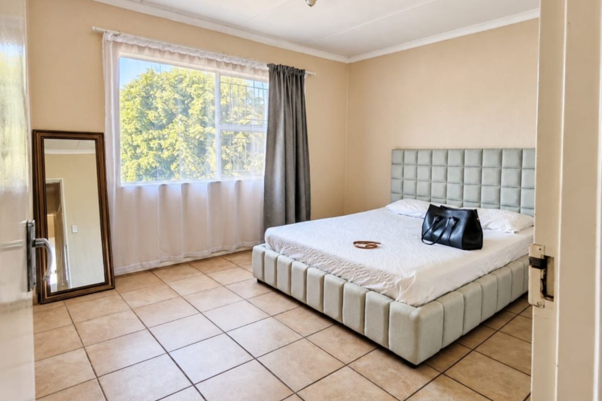 A bedroom featuring tiled flooring, a window with security bars, and a ceiling-mounted light fixture.