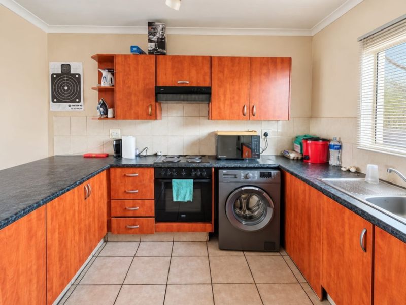 Functional kitchen featuring wood-look laminate cabinetry, dark countertops, integrated oven and hob, and tiled flooring with a neutral backsplash.