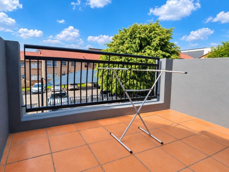 A clean, open-air balcony featuring terracotta-style floor tiles and a secure black metal balustrade overlooking the complex parking area.