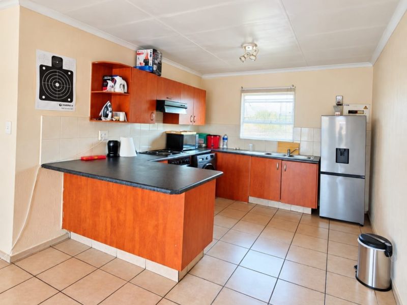 A functional kitchen featuring wood-look laminate cabinetry, dark countertops, tiled flooring, and a tiled backsplash with integrated cooking appliances.