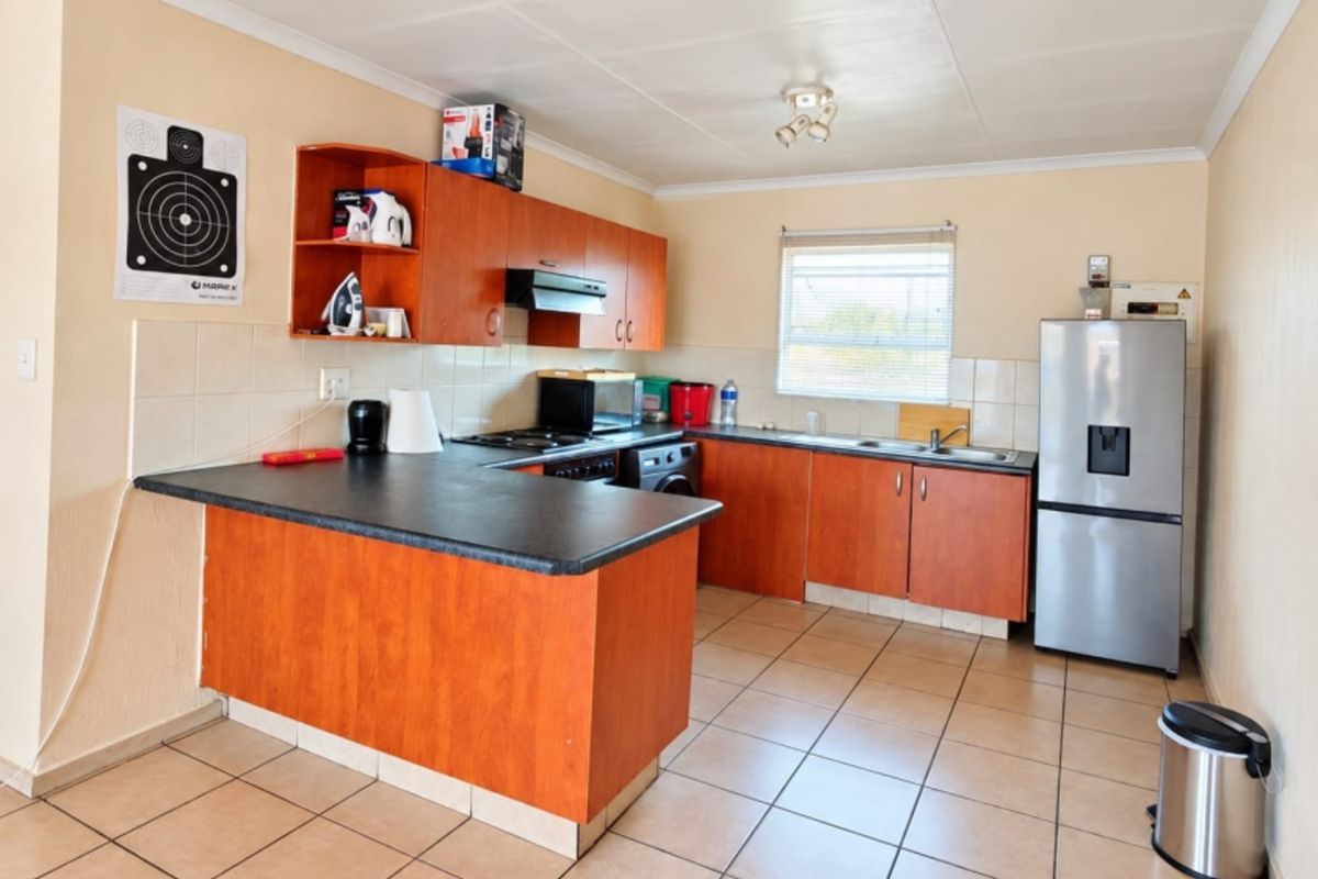 A functional kitchen featuring wood-look laminate cabinetry, dark countertops, tiled flooring, and a tiled backsplash with integrated cooking appliances.