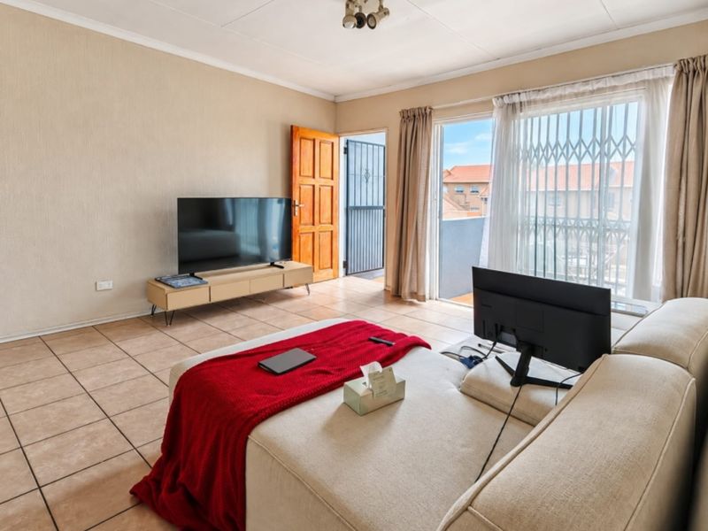 A living room featuring tiled flooring, a sliding glass door with security gate leading to a balcony, and a timber entrance door.