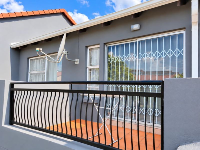 A private balcony featuring tiled flooring, a secure metal balustrade, and sliding glass doors with security gates, providing a functional outdoor space.