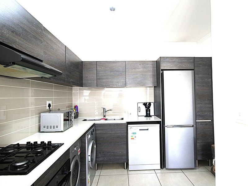Modern kitchen featuring dark wood-grain cabinetry, gas hob, extractor fan, tiled backsplash, and integrated space for appliances.