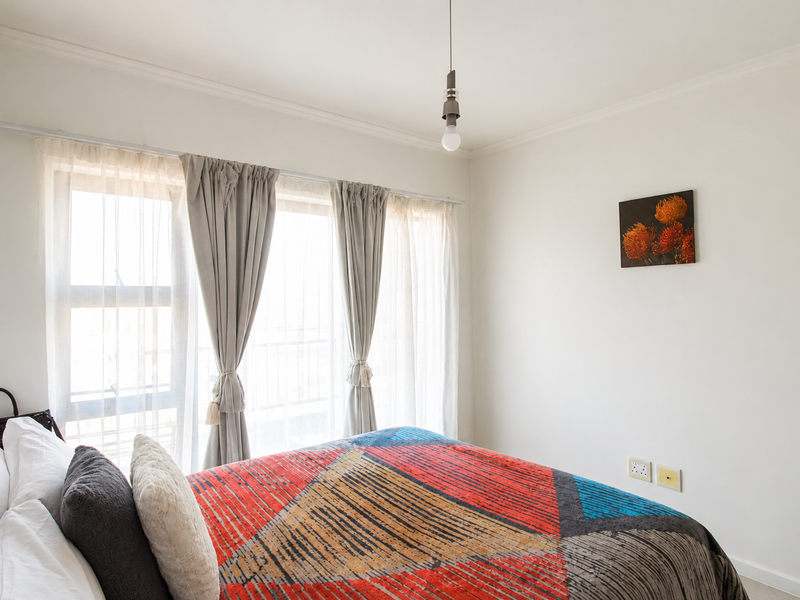 A bright bedroom featuring a large window with curtain rod, pendant lighting, and wall-mounted electrical outlets.