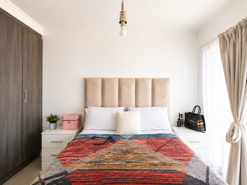 A well-maintained bedroom featuring a large built-in wardrobe, crown molding, and a central pendant light fixture, offering a clean and functional living space.
