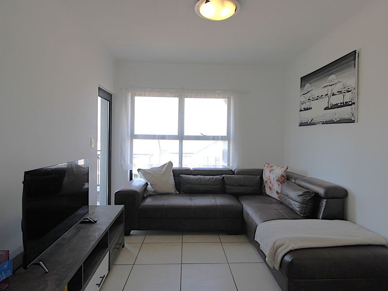 A well-maintained living room featuring neutral tiled flooring, a central ceiling light, and a sliding glass door providing natural light.