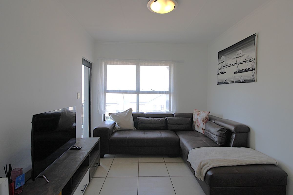 A well-maintained living room featuring neutral tiled flooring, a central ceiling light, and a sliding glass door providing natural light.