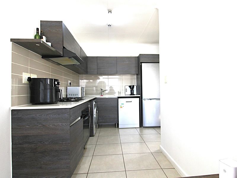 A functional kitchen featuring dark wood-grain cabinetry, a tiled backsplash, built-in oven, hob, extractor fan, and tiled flooring.
