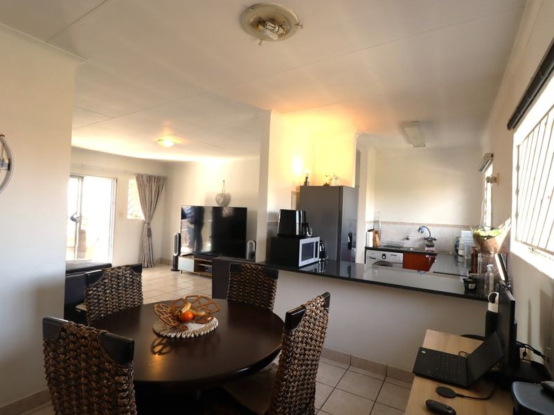 Open-plan living and dining area featuring tiled floors, a functional kitchen with granite countertops, and access to an outdoor space via sliding doors.