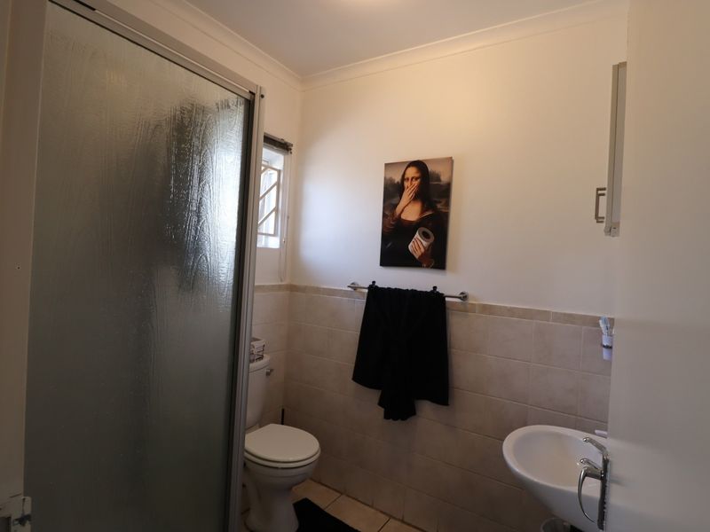 A functional bathroom featuring a shower enclosure, pedestal basin, and toilet with neutral wall tiling.