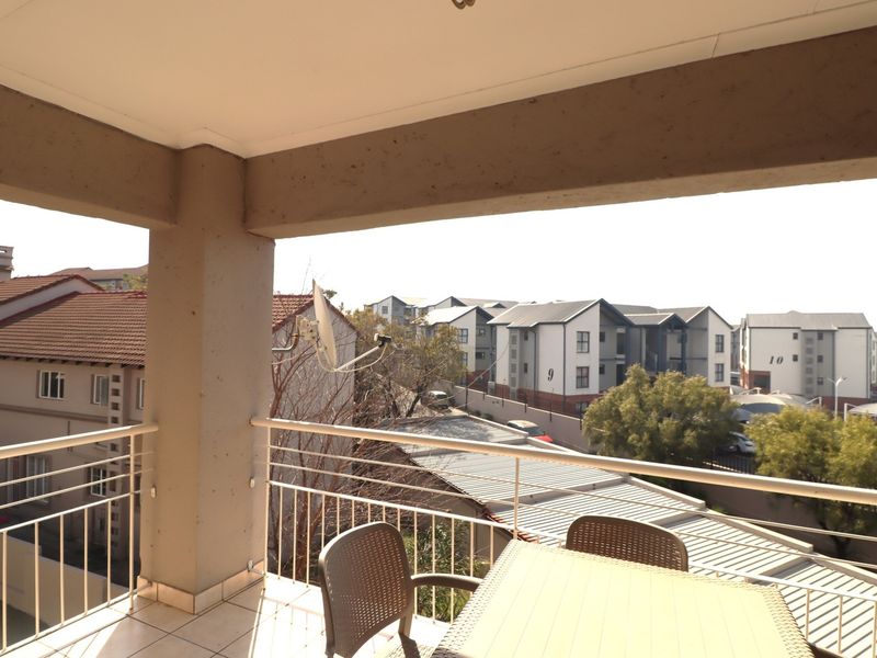 A covered balcony featuring tiled flooring and a metal balustrade, offering an elevated view of the surrounding residential complex.