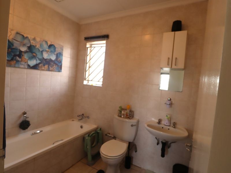 A functional bathroom featuring a bathtub, pedestal basin, toilet, and wall-mounted storage cabinet, finished with neutral wall tiles.