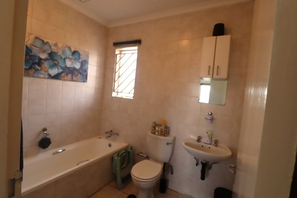 A functional bathroom featuring a bathtub, pedestal basin, toilet, and wall-mounted storage cabinet, finished with neutral wall tiles.