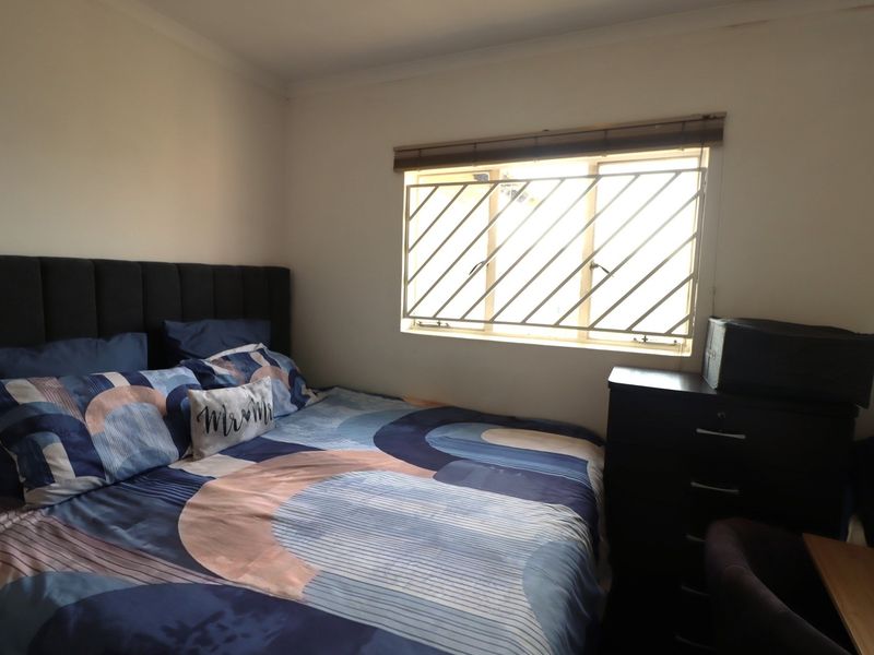 A functional bedroom featuring a window with fitted security bars and blinds, providing natural light and essential security.