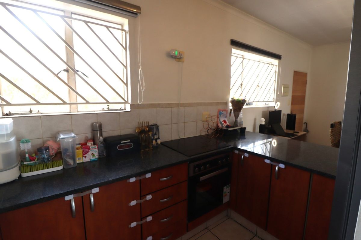 Functional kitchen featuring dark granite countertops, built-in oven and hob, tiled backsplash, and ample wooden cabinetry with security bars on the windows.