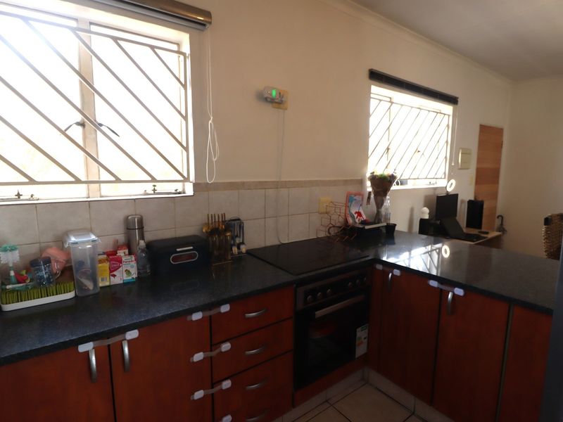 Functional kitchen featuring dark granite countertops, built-in oven and hob, tiled backsplash, and ample wooden cabinetry with security bars on the windows.