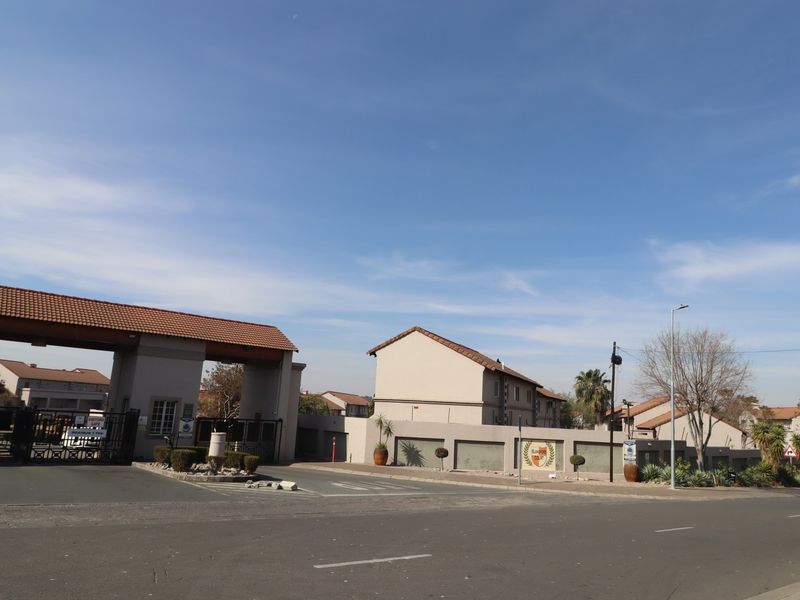 Street view of the apartment complex entrance featuring a secure gated access point and perimeter walling.