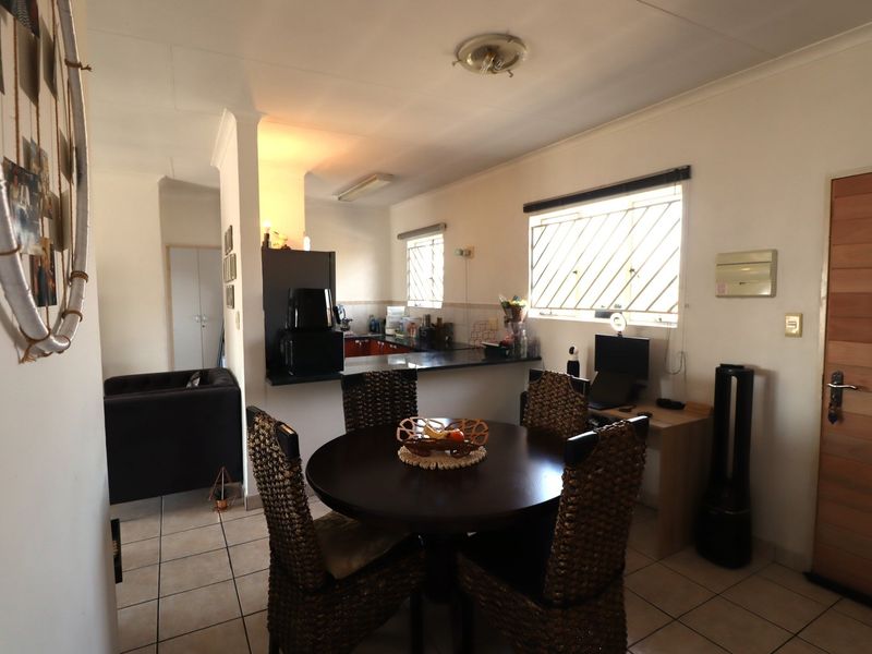Open plan living and dining area featuring tiled flooring, a functional kitchen with built-in cabinetry, and natural light through security-barred windows.