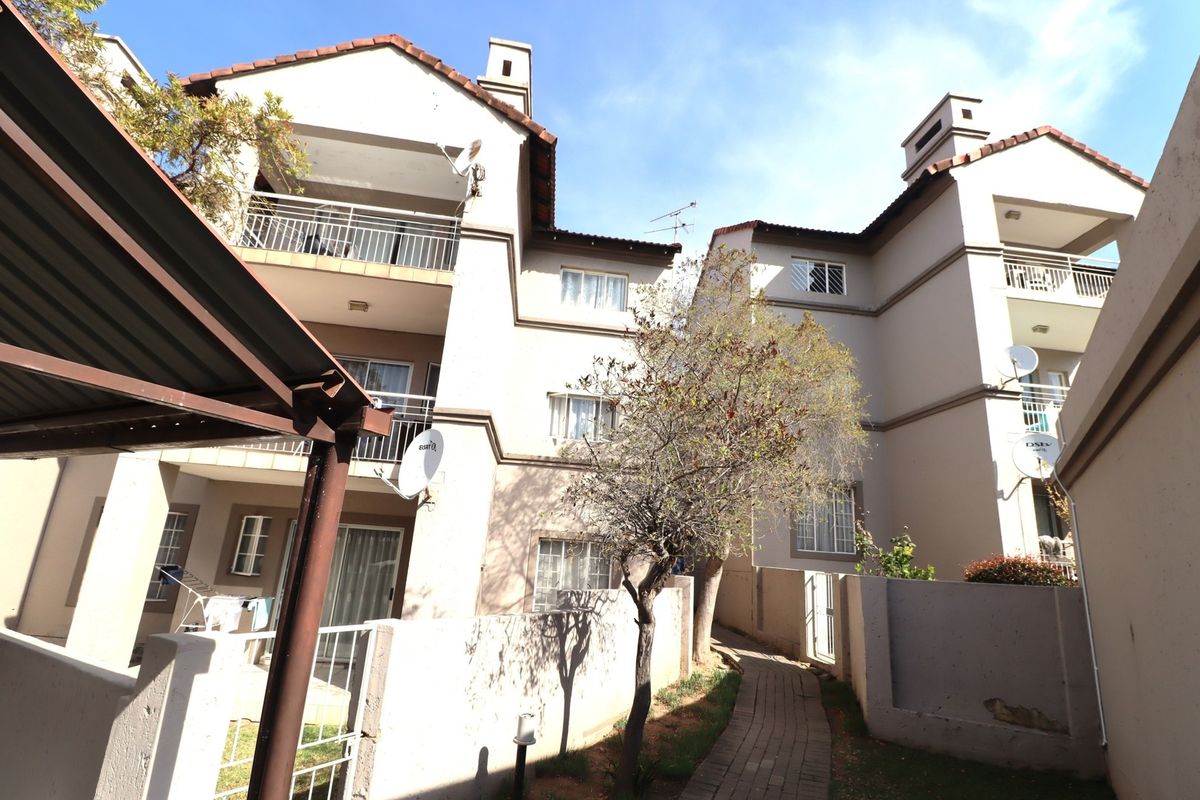 Rear view of a multi-story apartment complex featuring private balconies, paved walkways, and established exterior finishes.