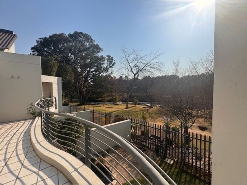 A spacious curved balcony featuring tiled flooring and metal railings, offering an elevated view of the surrounding garden and landscape.