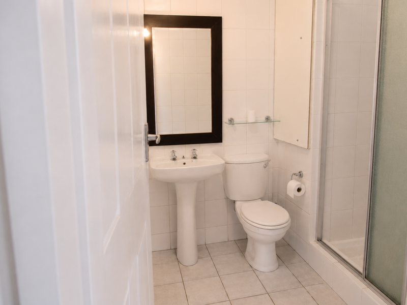 A functional bathroom featuring a pedestal basin, toilet, and a glass-enclosed shower with neutral wall and floor tiling.