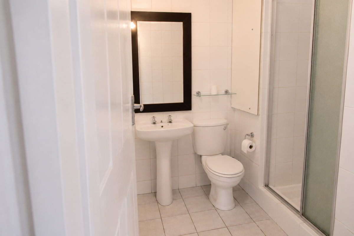 A functional bathroom featuring a pedestal basin, toilet, and a glass-enclosed shower with neutral wall and floor tiling.