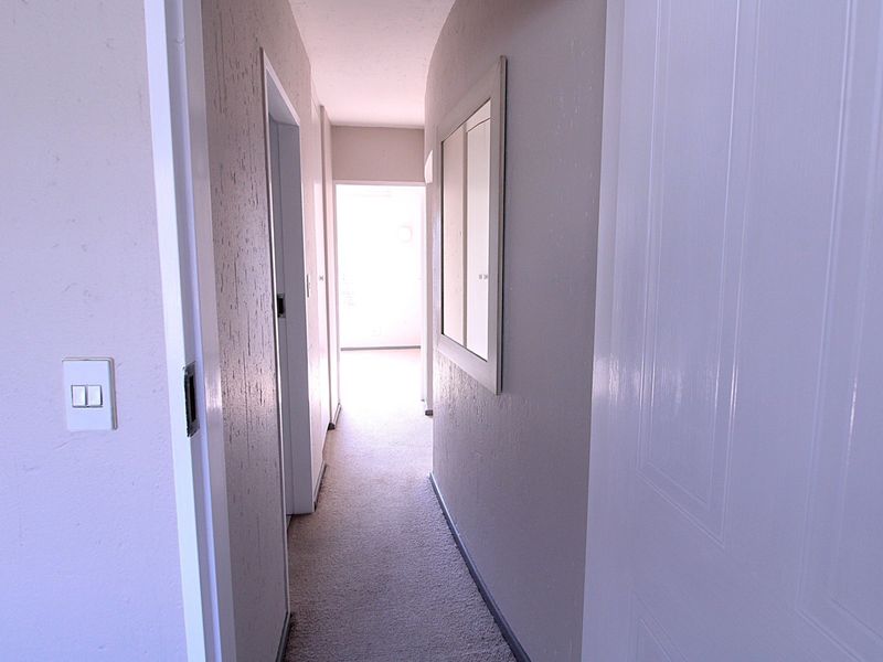 A functional hallway connecting interior spaces, featuring neutral wall finishes, carpeted flooring, and multiple internal door access points.