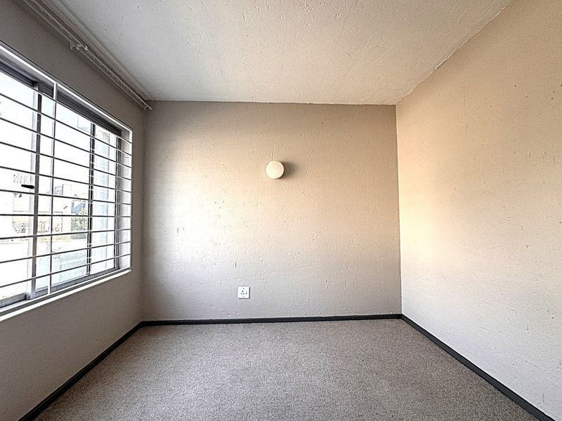 A vacant bedroom featuring neutral walls, carpeted flooring, and a window fitted with security bars, providing a blank canvas for personalization.
