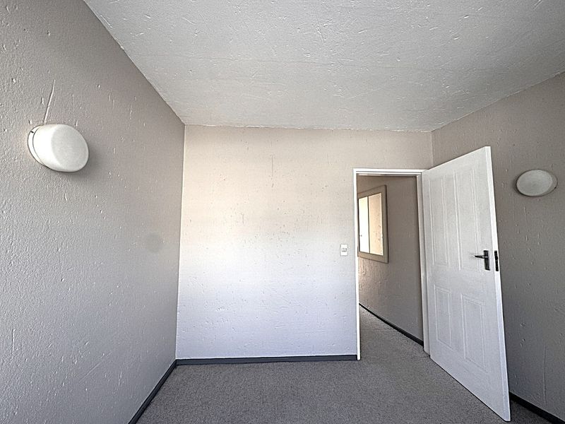 An empty bedroom featuring neutral wall finishes, carpet flooring, and two wall-mounted light fixtures, providing a blank canvas for potential interior design.