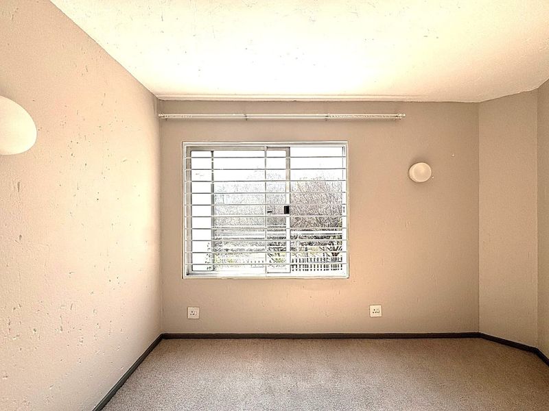 An empty bedroom featuring a sliding window with security bars, carpeted flooring, and wall-mounted lighting fixtures.