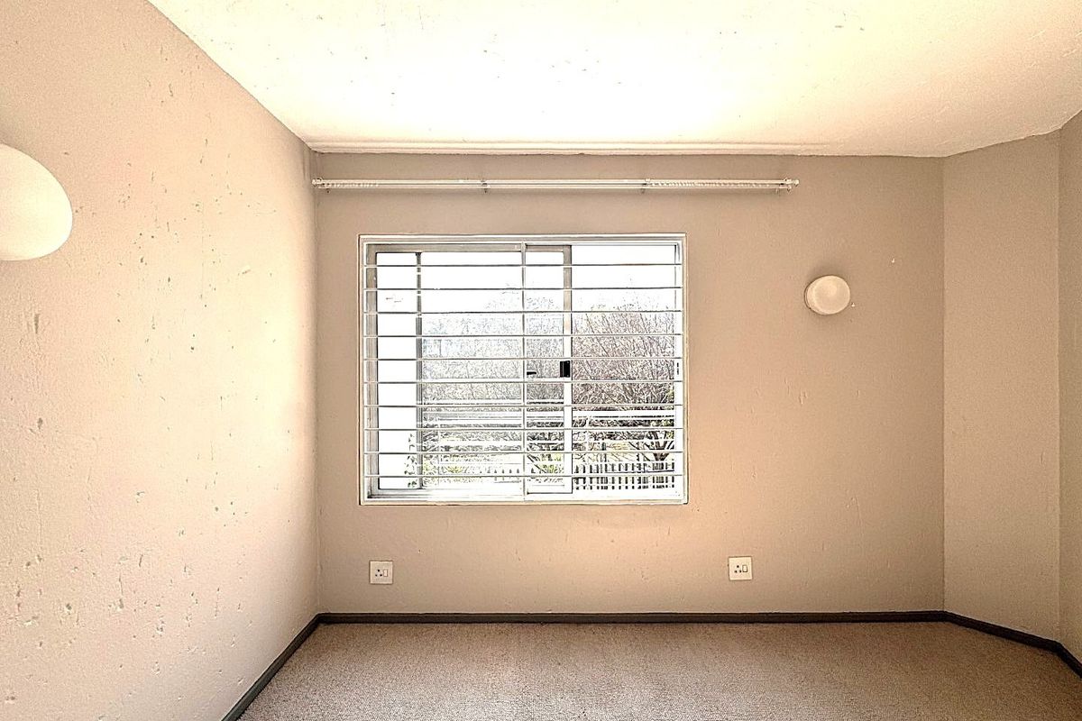 An empty bedroom featuring a sliding window with security bars, carpeted flooring, and wall-mounted lighting fixtures.