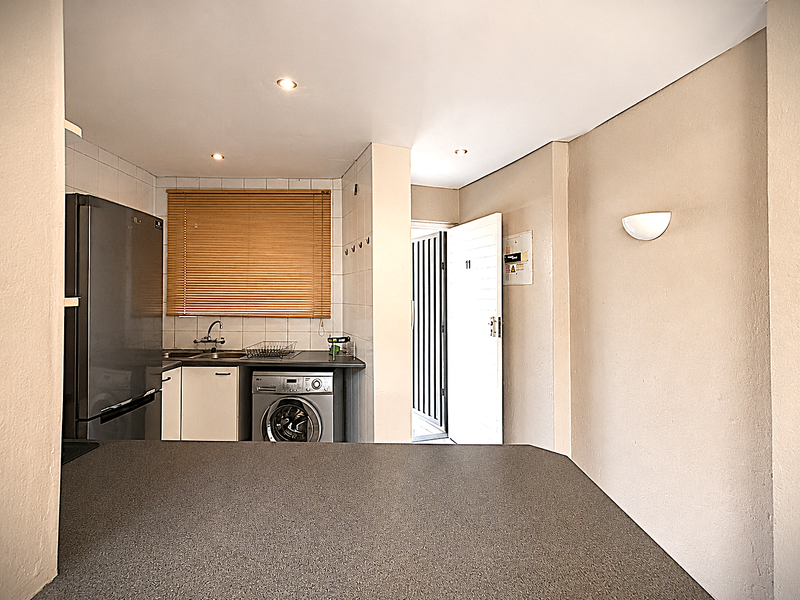 Compact kitchen area featuring built-in cabinetry, laminate countertops, stainless steel sink, and integrated laundry appliance space, with direct access to the entrance.