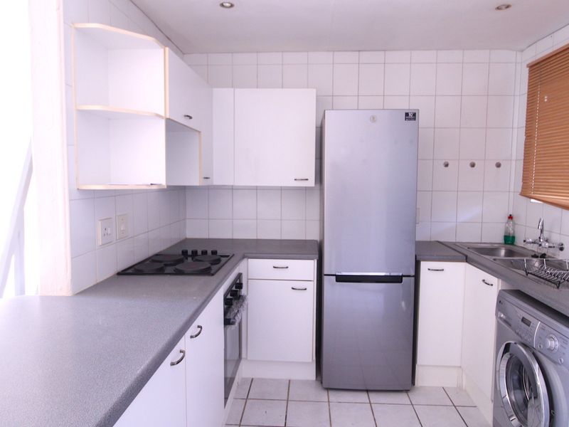 Functional kitchen featuring white cabinetry, laminate countertops, built-in oven and hob, tiled splashbacks, and dedicated space for laundry appliances.
