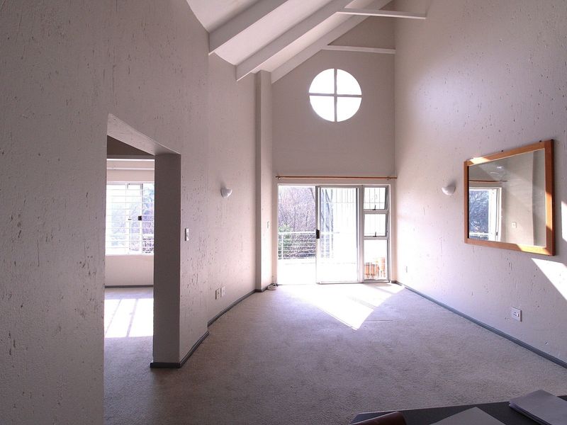 Spacious living area featuring a high vaulted ceiling with exposed rafters, a unique circular window, and sliding glass doors leading to an outdoor space.