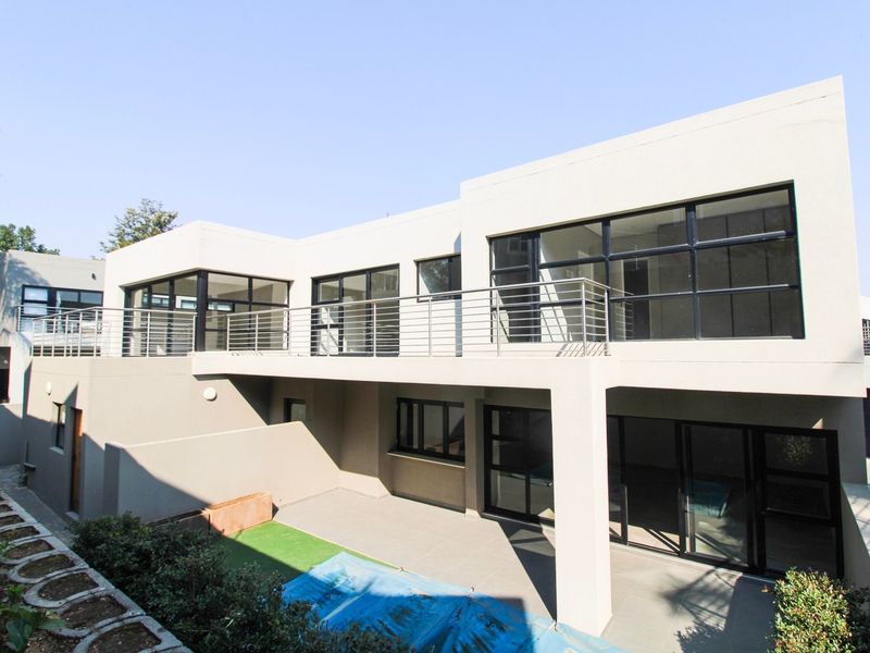 Modern rear elevation featuring a spacious tiled patio, large aluminium-framed windows, and an upper-level balcony with a sleek stainless steel balustrade.
