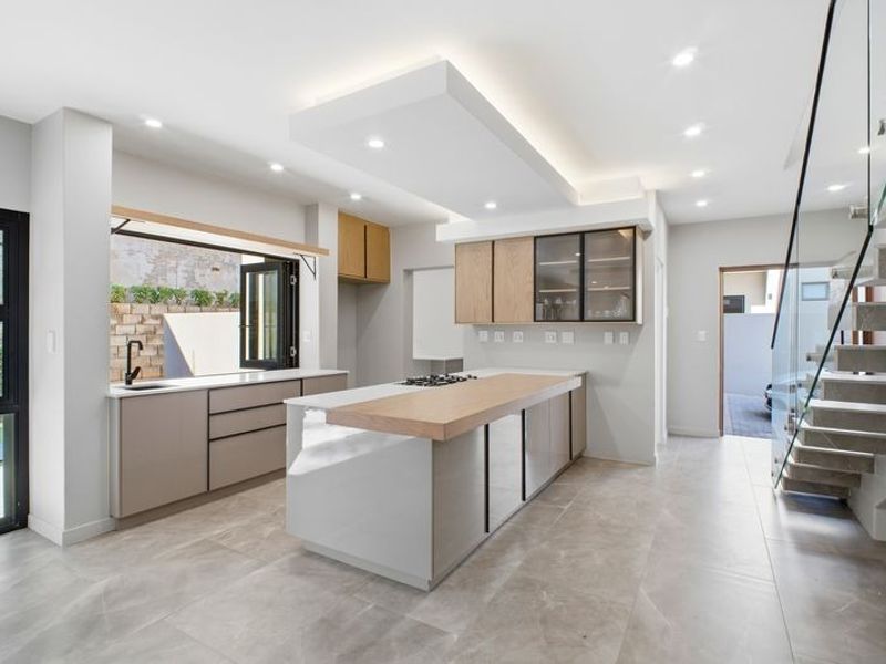 Modern open-plan kitchen featuring a central island with gas cooktop, sleek cabinetry, stone countertops, and direct access to an outdoor area via bi-fold windows.