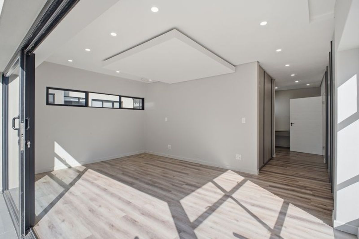 A bright, modern, and empty bedroom featuring laminate flooring, a contemporary drop ceiling with recessed lighting, built-in cupboards, and large sliding glass doors.