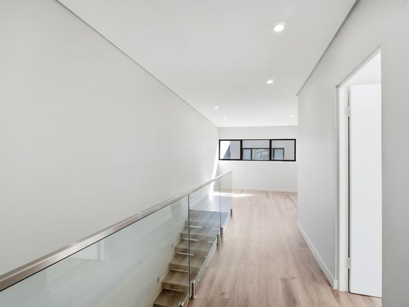 A bright and modern hallway featuring timber flooring, a sleek glass balustrade overlooking the staircase, and recessed downlighting.