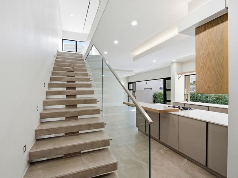 Modern open-plan living area featuring a striking stone staircase with glass balustrade, sleek kitchen cabinetry, and high-end finishes throughout.