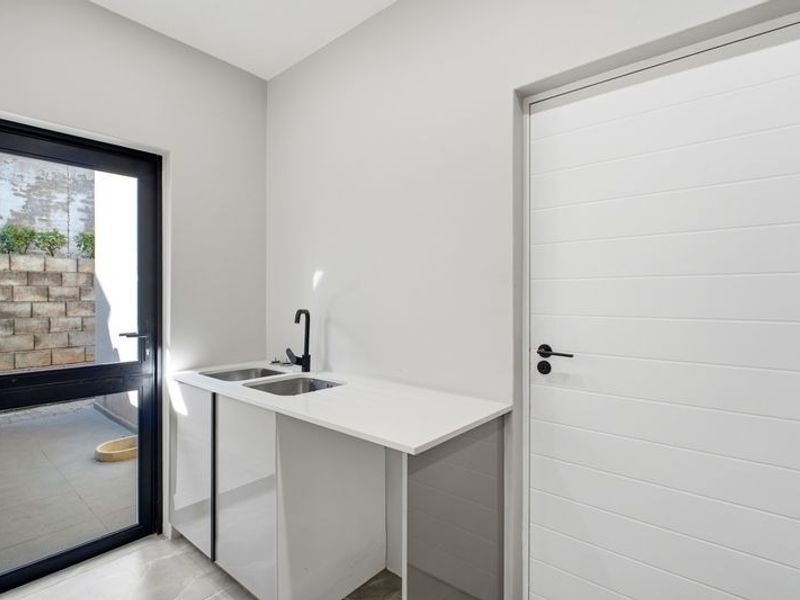 A clean, modern laundry area featuring built-in cabinetry, a stainless steel sink with a black mixer tap, and direct access to an outdoor patio.