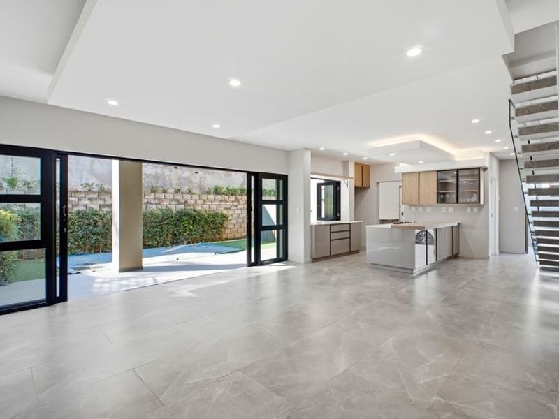 Spacious open-plan living and kitchen area featuring modern cabinetry, a central island, large sliding doors to the patio, and a contemporary staircase.