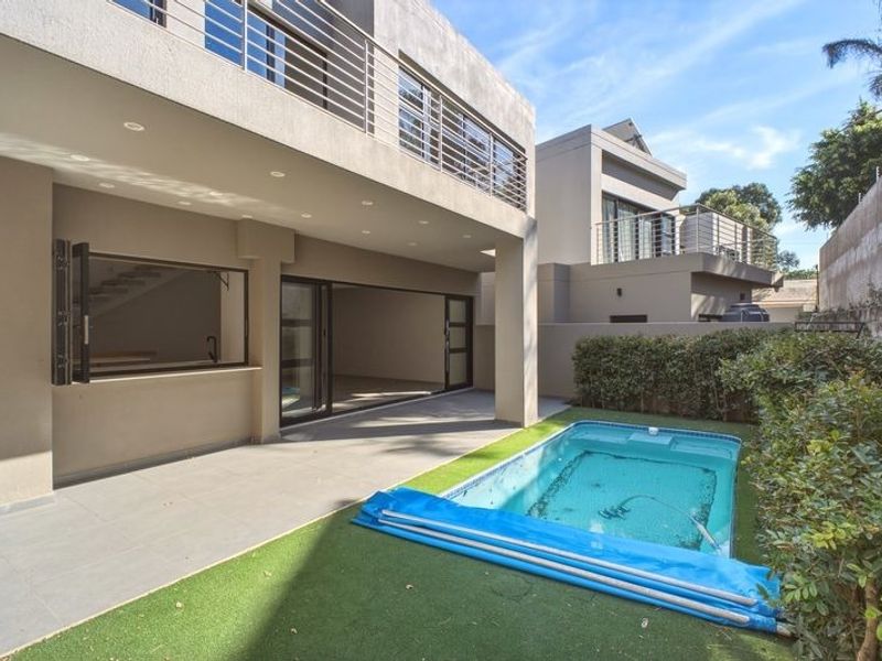 Rear exterior view featuring a covered patio, swimming pool with cover, and a balcony overlooking the garden area.